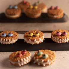 Detailne foto vegan Halloweeni koletisküpsistest, mis on kaunistatud värvilise glasuuri, nööpide ja šokolaadilaastudega, asetatud puidust lauale.