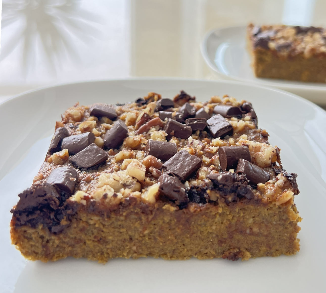 Kõrvitsa-õuna piparkoogikook šokolaadi ja pähklitega – gluteenivaba tervislik kook Gluteenivaba kõrvitsa-õuna piparkoogikook šokolaadinööpide ja pähklitega valgel taldrikul.